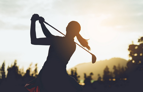 Silhouette of woman golfing with sunset on horizon