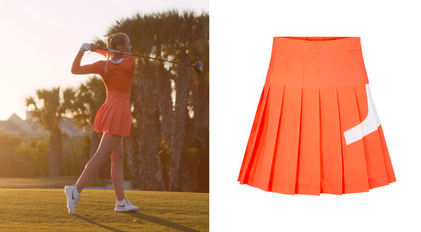 LPGA golfer Nelly Korda swings golf club in orange outfit surrounded by trees and grass with hazy filter